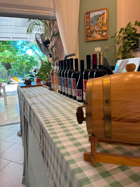 חבית עץ קטנה עם ברז לצד שורת בקבוקי יין בחלל הטעימות של היקב, עם מבט אל הגינה