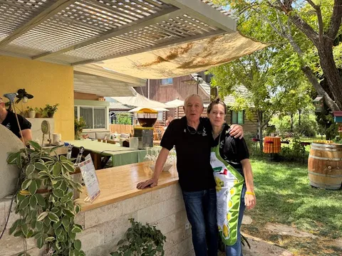 בעלי יקב סודות עומדים מחויכים ליד בר העץ תחת הפרגולה בחצר היקב במושב תימורים