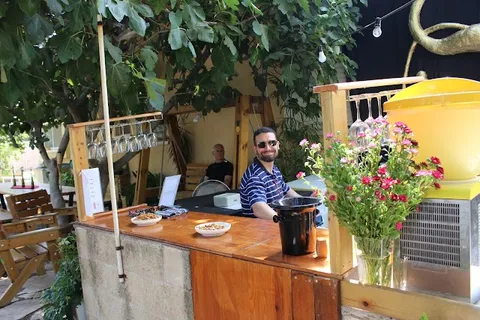 עמדת המזיגה בחצר היקב עם זר פרחים טרי ומארח מחייך מאחורי הבר