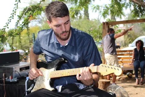 נגן גיטרה חשמלית מופיע בהופעה חיה בין עצי החצר באירוע ביקב